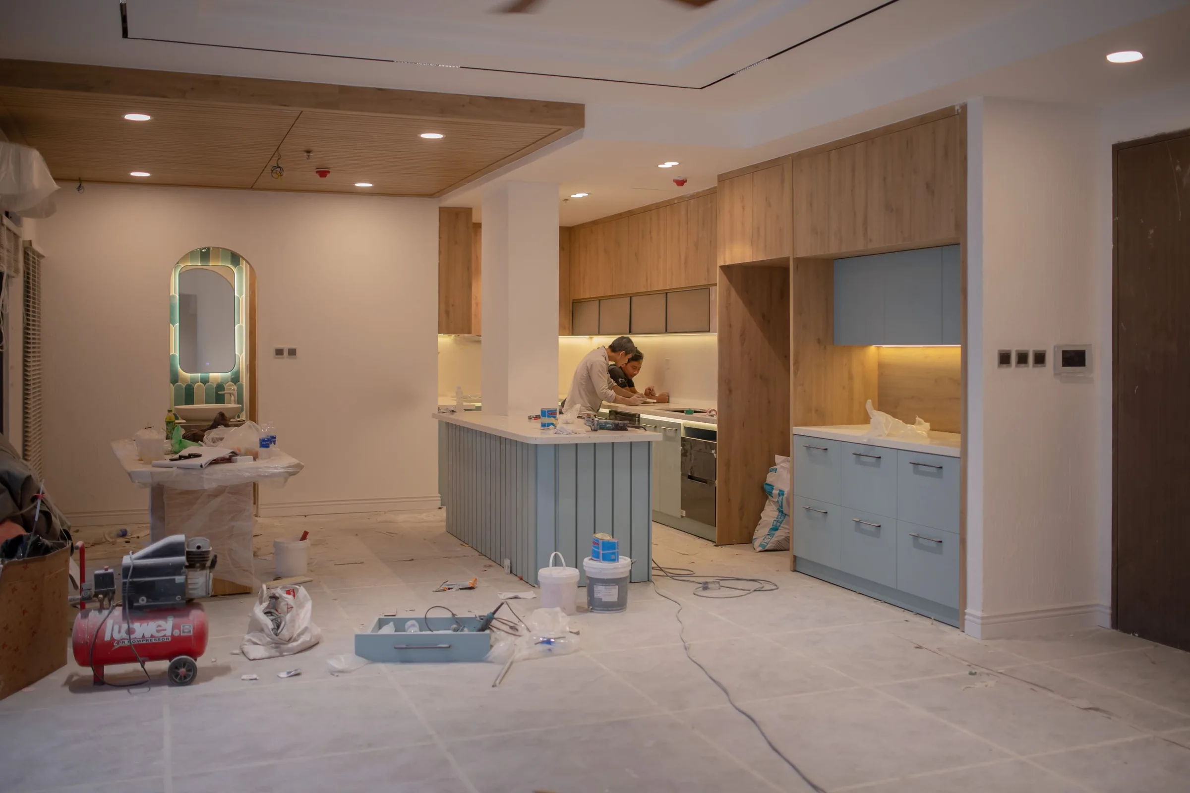 Kitchen under renovation with wood cabinets, a blue island, a worker and tools on the unfinished floor