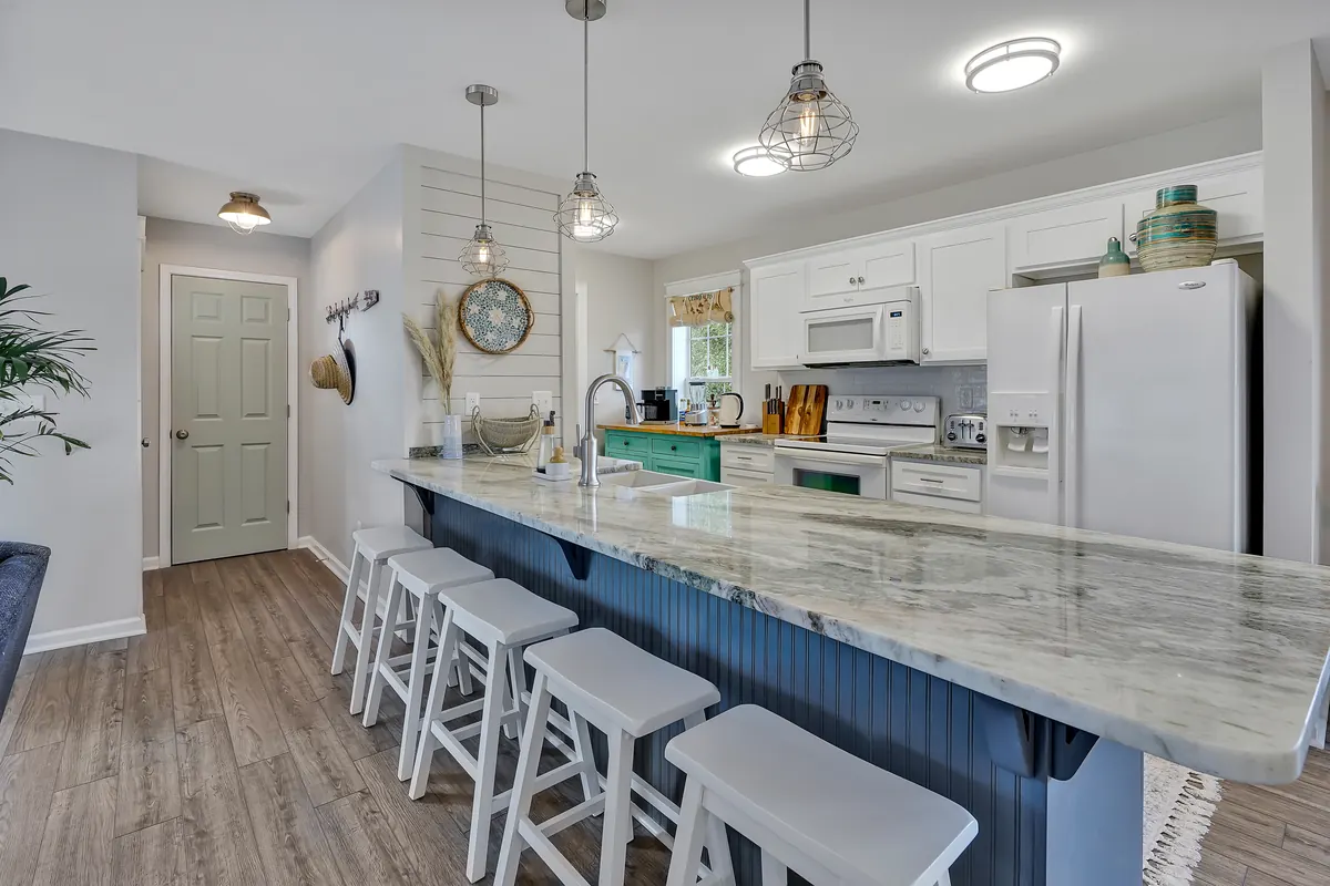 Kitchen with white cabinets and appliances, a stainless steel sink, a long stone counter and a blue island with white stools