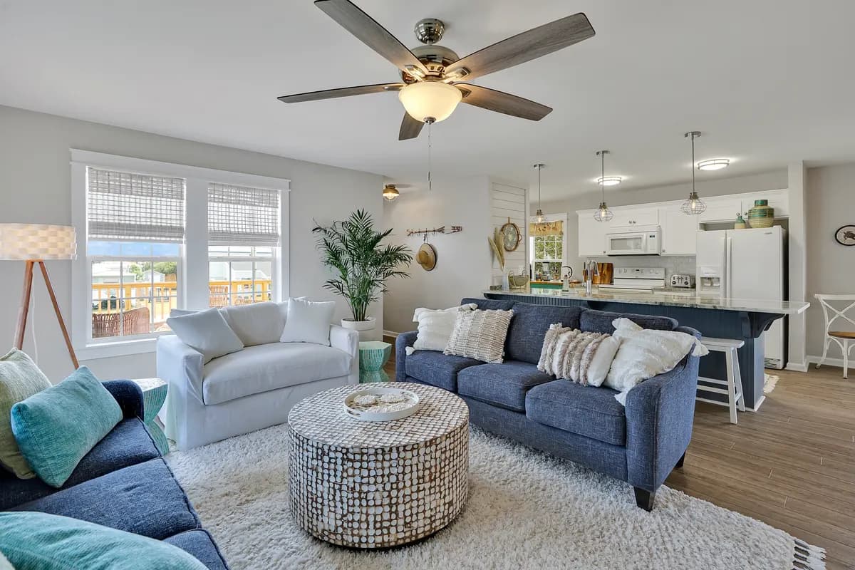 Open living room with white and navy sofas, a round coffee table and a kitchen island behind them