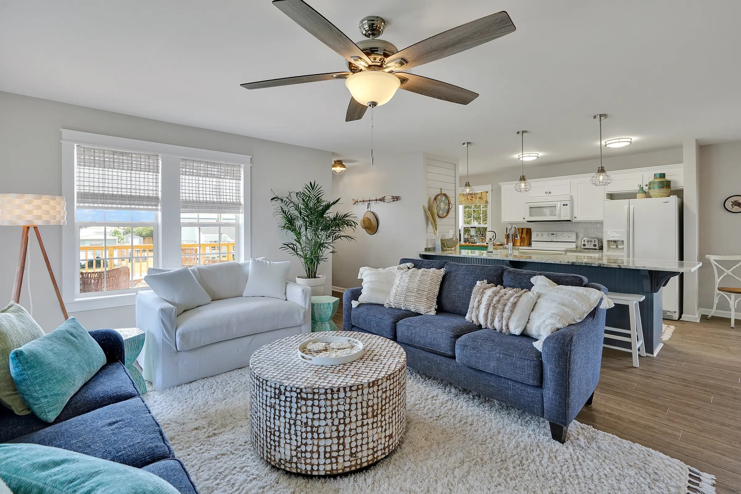 Open living room with white and navy sofas, a round coffee table and a kitchen island behind them